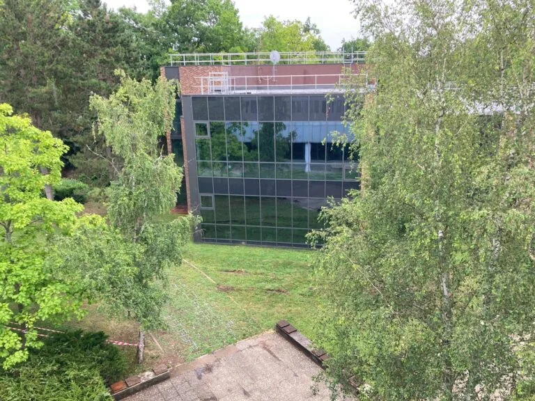 A modern building with a glass façade, surrounded by green trees