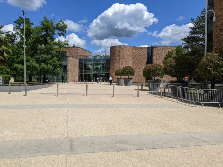 The façade of a modern brick building with a sunny esplanade