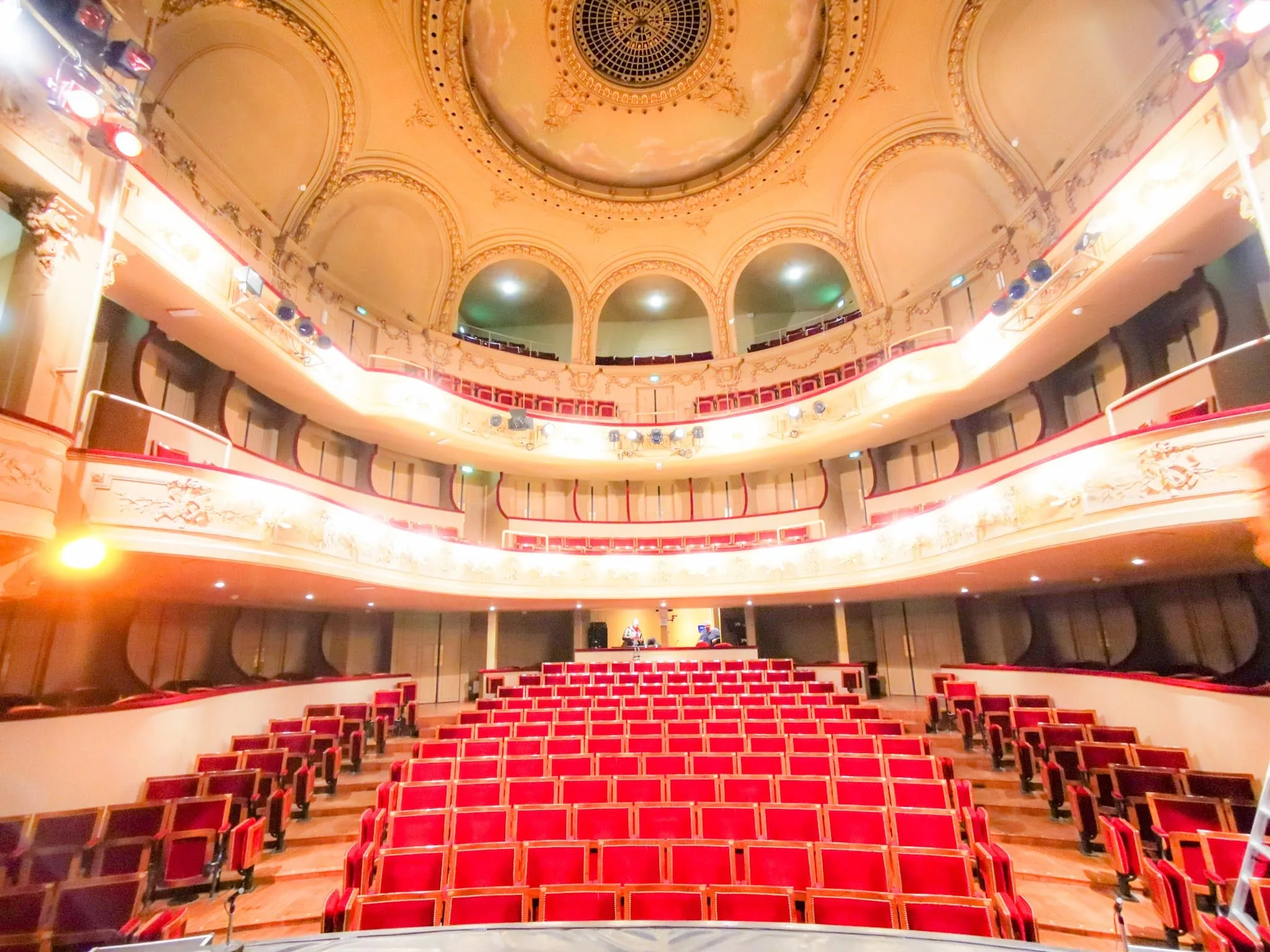 A traditional theatre with red armchairs and an ornate ceiling