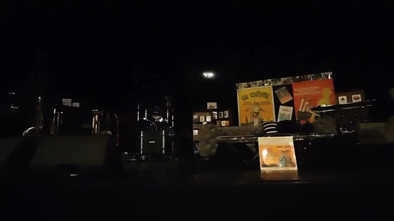 A dark scene featuring posters of French films, including *La Chèvre*