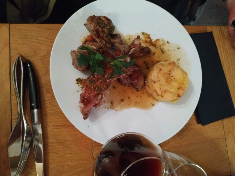 Pièce d'agneau rôtie aux herbes avec gratin dauphinois sur assiette blanche et verre de vin rouge – Le Mécano Fontainebleau