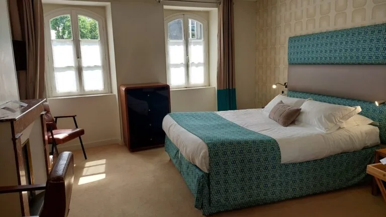 Zimmer im Hotel Victoria Fontainebleau mit türkisfarbenem Doppelbett, zwei Spitzbogenfenstern und Vintage-Möbeln