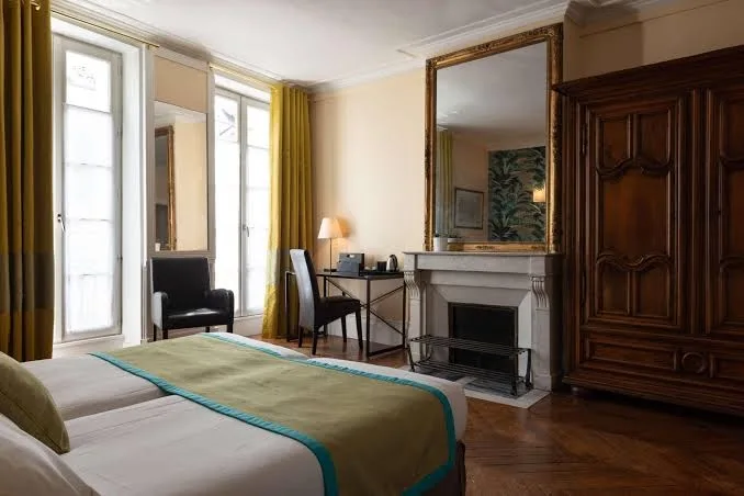 Klassisches Zimmer im Hotel Victoria Fontainebleau mit Doppelbett, Kamin, Holzschrank und gelben Vorhängen