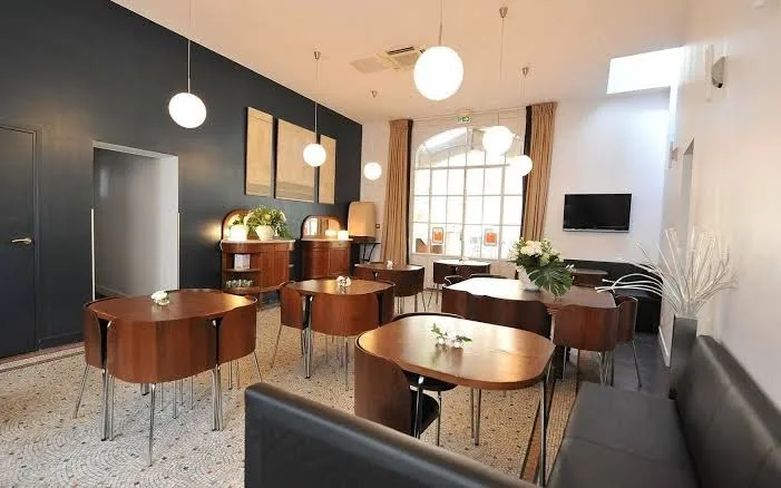 Frühstücksraum im Hotel Victoria Fontainebleau mit runden Holztischen, kugelförmigen Pendelleuchten und gewölbtem Fenster