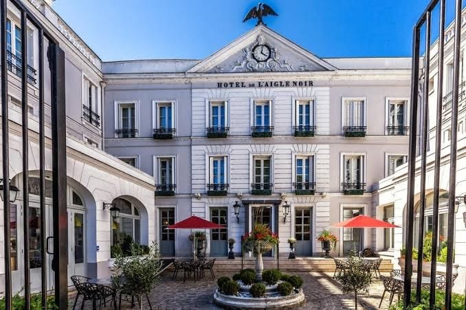 Façade et cour intérieure de l’hôtel Aigle Noir à Fontainebleau avec fontaine centrale