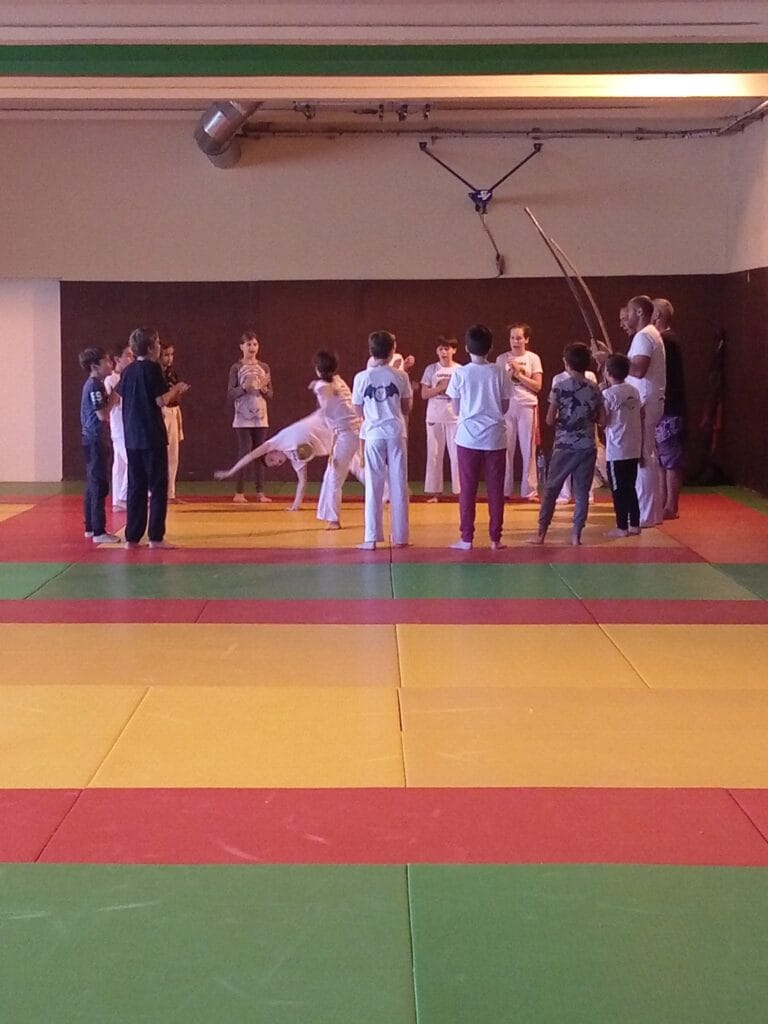 Cours de capoeira pour enfants au Complexe Sportif de la Vallée, pratiquants en cercle sur tatamis colorés