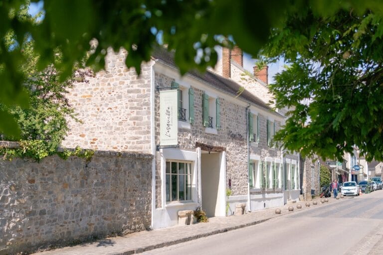 Exterior facade of the Esquisse Hôtel Culturel in Fontainebleau, a stone building with green shutters framed by vegetation.