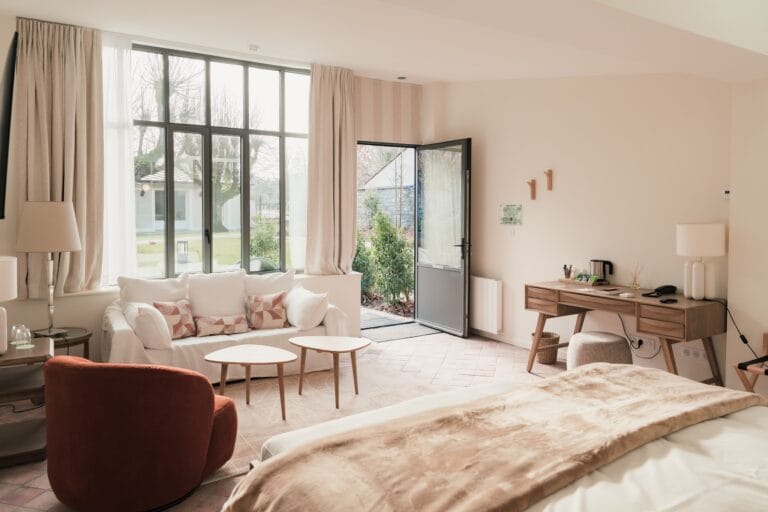 Suite at l'Esquisse Hôtel Culturel in Fontainebleau, large space with white sofa, brick-red armchair and garden access