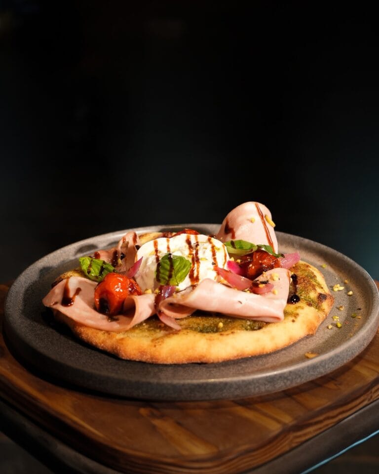 Focaccia garnie de jambon, burrata, tomates confites, basilic et réduction balsamique sur assiette en pierre – L'Office Fontainebleau