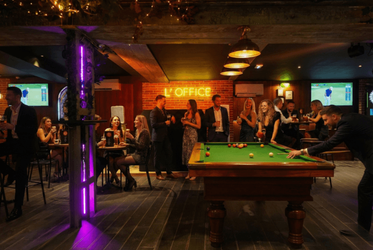 Ambiance festive à L'Office bar avec clients autour du billard, enseigne néon L'OFFICE et écrans