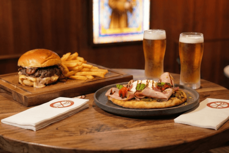 Table de l'Office avec burger-frites sur planche en bois, focaccia jambon-burrata et deux bières pression