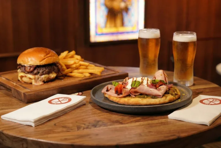 Table de l'Office avec burger-frites sur planche en bois, focaccia jambon-burrata et deux bières pression