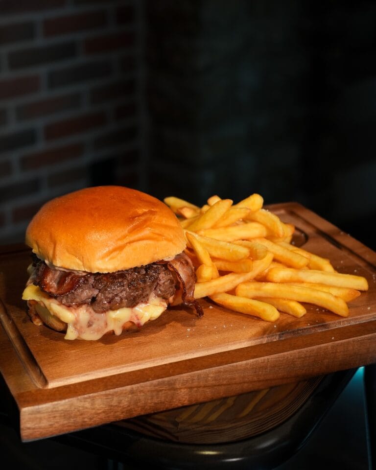 Burger généreux avec fromage fondu et bacon servi sur planche en bois avec frites – L'Office bar à jeux de Fontainebleau