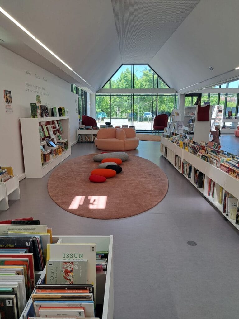 Light-filled interior of the Les Sources Vives multimedia library in Avon, with round carpet, colourful poufs and a large glass roof.