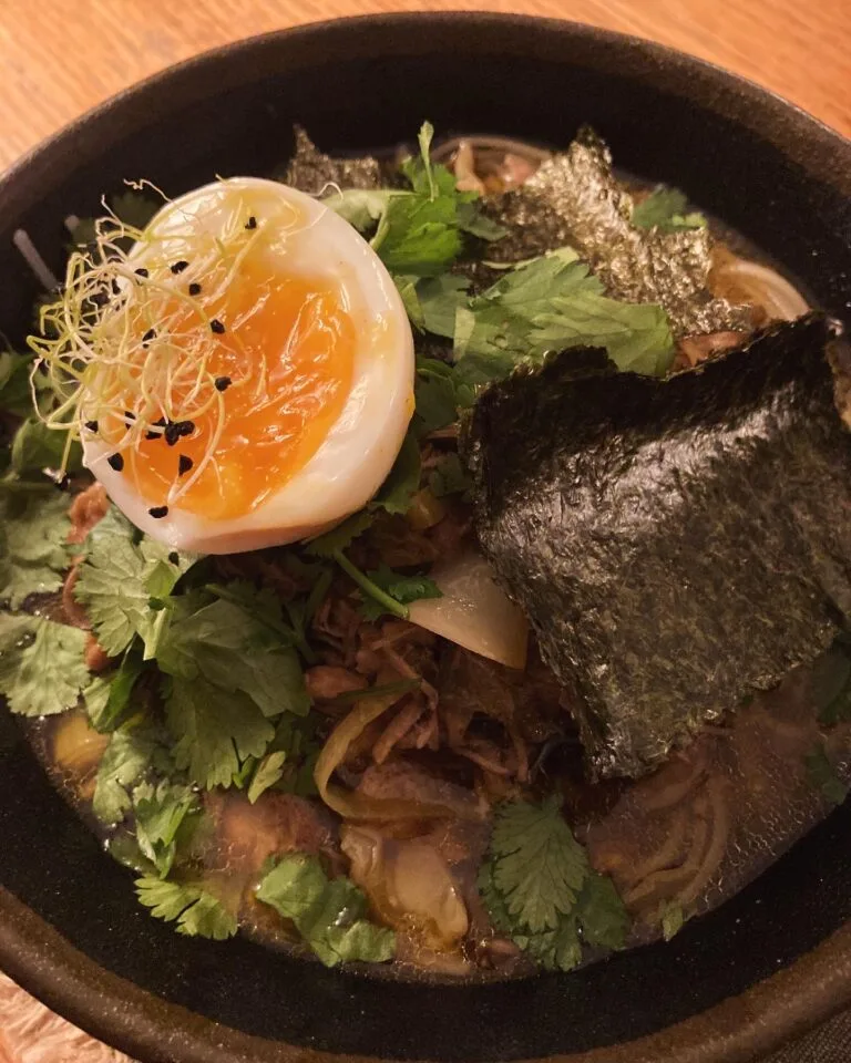 Homemade ramen with soft-boiled egg, nori, coriander and sprouted seeds in a black bowl