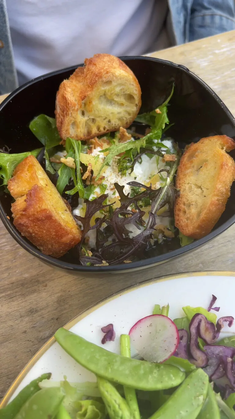 Burrata, rocket and golden croutons salad served in a black bowl at Maison Sumac