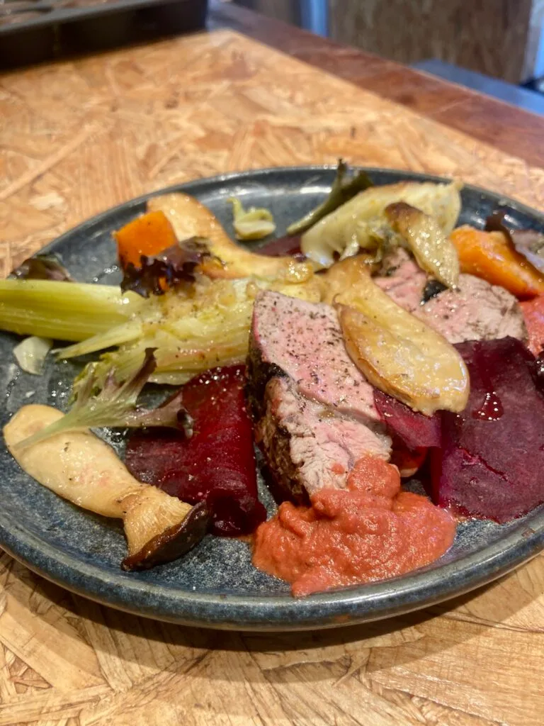 Sliced pink meat with roast vegetables, beetroot and purée on a blue stoneware plate