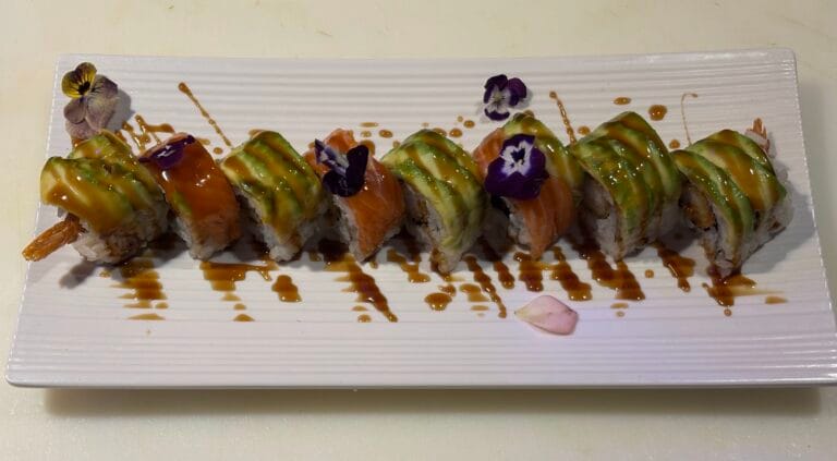 Lachs- und Avocadomaki-Maki mit essbaren Blüten und Teriyaki-Sauce, sorgfältige Präsentation
