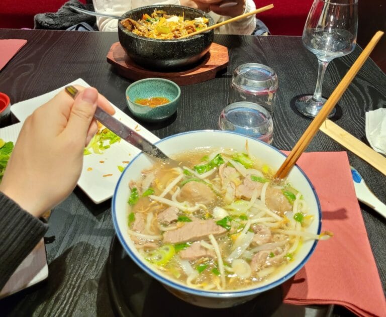 Pho-Suppe mit Rindfleisch, Sojasprossen und frischen Kräutern, Bibimbap im Hintergrund