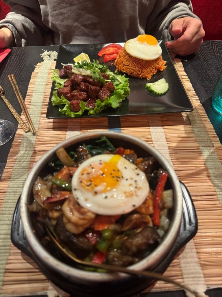 Tisch mit Bibimbap aus heißem Stein und Teller mit gegrilltem Fleisch und gebratenem Reis