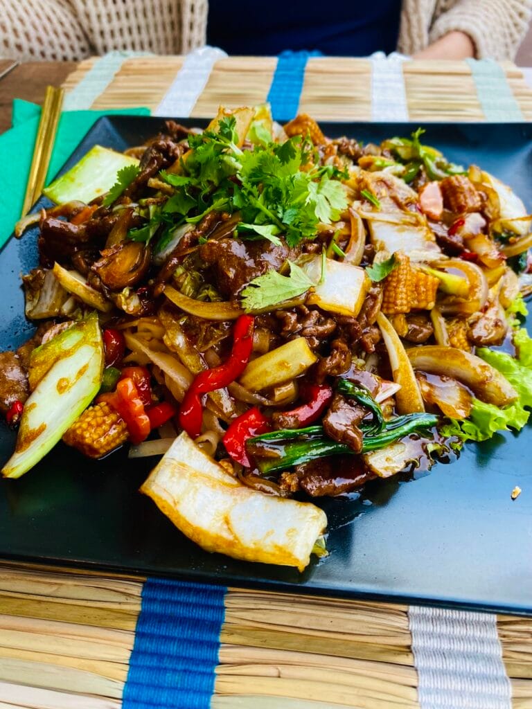 Wok mit sautiertem Rindfleisch, Gemüse, Mini-Maiskölbchen und Paprika, serviert auf der Terrasse