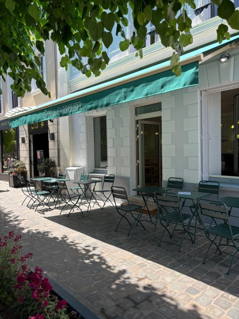 The sunny terrace of the Café du Carrousel with green chairs