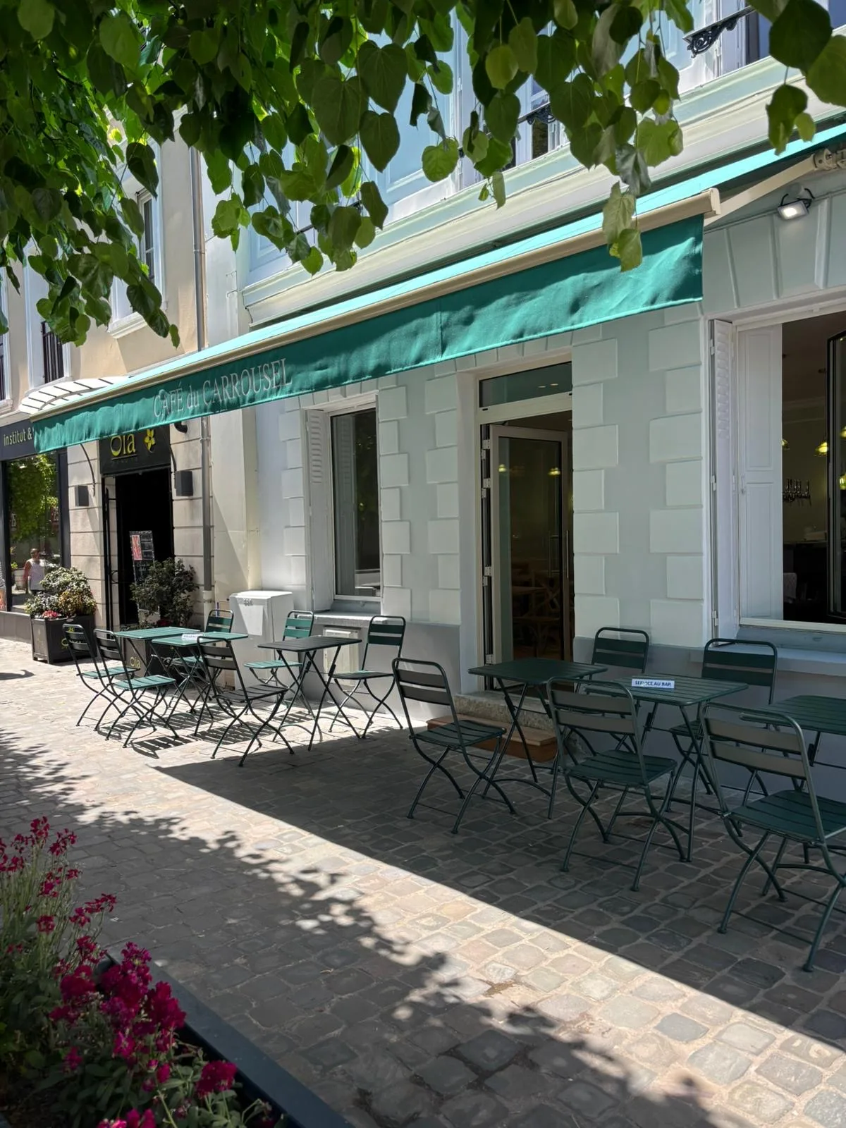 Terrasse ensoleillée du Café du Carrousel avec chaises vertes