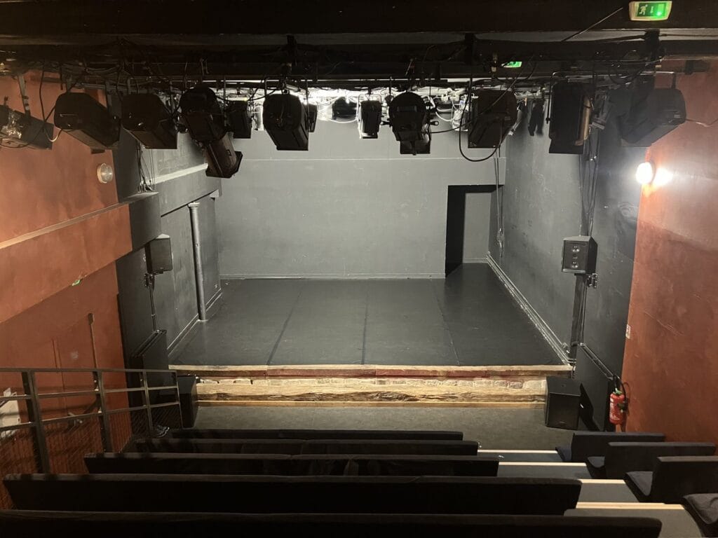 La salle de 74 places de l'Âne Vert Théâtre vue du haut du gradin, plateau nu et projecteurs